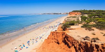 Layered red and orange sandstone cliffs rising above golden sand at Praia da Falésia
