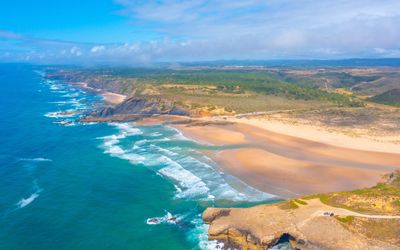 Wide sandy shoreline of Praia da Amoreira backed by dunes and dark cliffs
