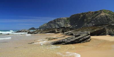 Praia da Carriagem's golden sand with dark schist rock formations and towering cliffs with seabirds