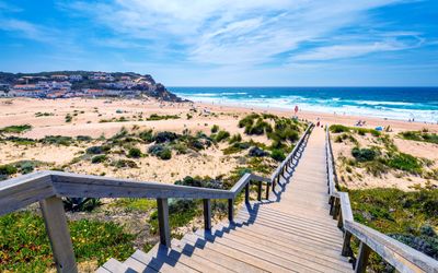 Wooden boardwalk with steps leading down through dunes towards the beach and ocean with the village in the background