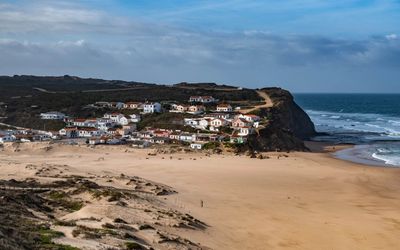 Monte Clérigo village with whitewashed houses and terracotta roofs clustered on a clifftop beside the sandy beach