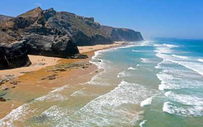 Dark rock formations and low scrub-covered cliffs at Praia de Vale Figueiras