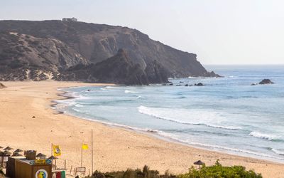 Wide golden beach at Praia do Amado framed by dramatic cliffs
