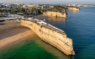 Aerial view of the whitewashed Nossa Senhora da Rocha chapel on a dramatic limestone promontory with beaches on either side