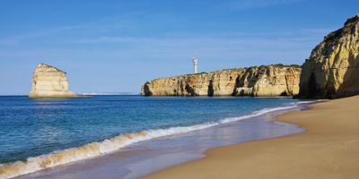 View along Praia dos Caneiros with golden sand stretching between ochre cliff walls