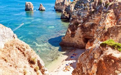 Kayakers on a tiny golden sand cove beach beneath dramatic ochre cliffs at Ponta da Piedade