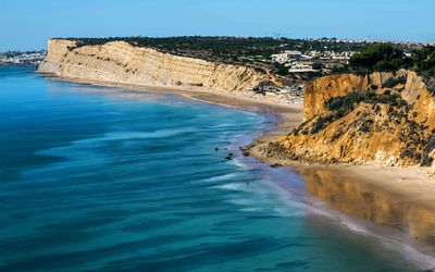 Elevated view of the beach curving around dramatic white and golden layered cliffs with turquoise water