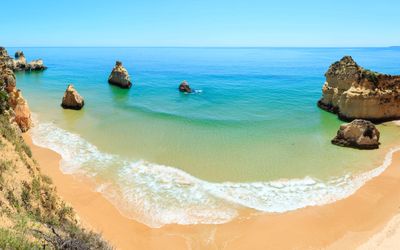Sheltered cove with golden sand, turquoise water, and tall sea stacks rising from the water between cliffsides