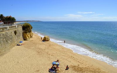 Long stretch of golden sand with a stone seawall, scattered rock formations, and calm turquoise water