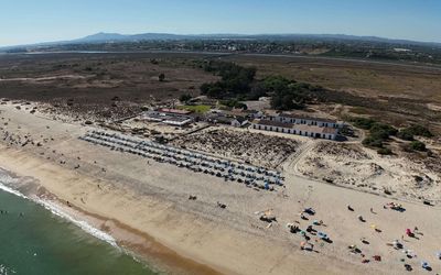 Aerial view of Praia do Barril on Ilha de Tavira, showing the golden sand beach, turquoise waters, and the Ria Formosa lagoon behind