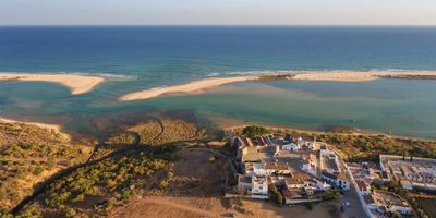 Praia de Cacela Velha stretching along the barrier island with the clifftop village visible in the distance