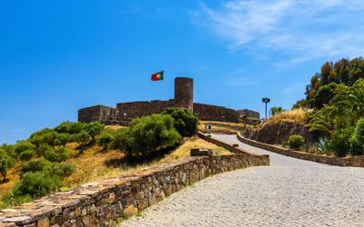 Cobbled pathway leading up to Aljezur Castle with its stone walls and round tower flying the Portuguese flag