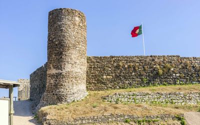 Close-up of the round stone tower and defensive walls of Aljezur Castle with the Portuguese flag flying behind