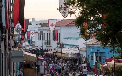 Crowded street during the Castro Marim Medieval Festival with Order of Christ banners, market stalls, and visitors