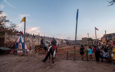 Jousting tournament at the Castro Marim Medieval Festival with an armoured knight on horseback in the castle arena at dusk