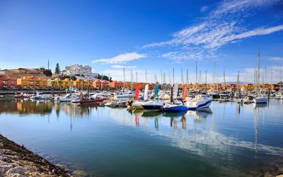 Portimão marina filled with sailboats and motorboats reflected in calm water with the town rising on the hillside behind