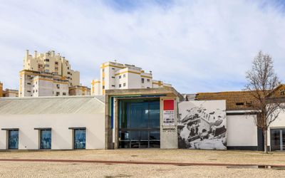 Museu de Portimão entrance with modern glass facade, exhibition banner, and a large black-and-white mural of fishing boats on the wall