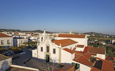 Aerial view of São Brás de Alportel's whitewashed Baroque church and terracotta rooftops with the Barrocal hills beyond