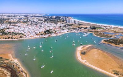 Aerial view looking east over the Alvor estuary with boats, sandbanks, the village, and Praia da Rocha in the distance