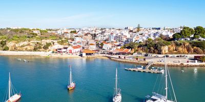 Aerial view of Alvor village with whitewashed houses, fishing harbour, sailboats, and a wooden jetty