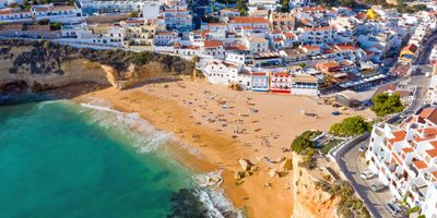 Carvoeiro's golden beach in a cove between ochre cliffs, with whitewashed houses cascading down the slopes above