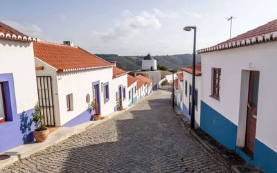 Cobbled street climbing through Odeceixe with colourful painted houses and the village windmill visible on the hilltop