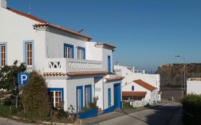 Traditional whitewashed houses with blue-trimmed windows and terracotta roofs lining a street descending towards the coast